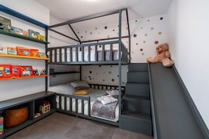 Una camera con un letto a castello, un orsetto di peluche, mensole con libri e una parete a pois.