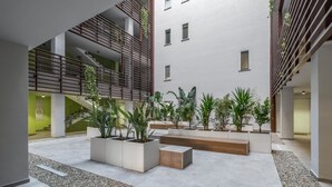 En moderne indre gårdhave med et centralt siddeområde, omgivet af plantekasser og en trappe.