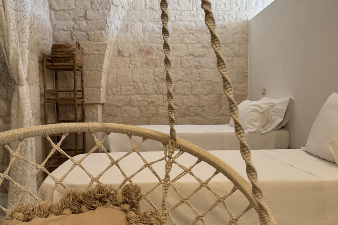 Une pièce avec un lit, une chaise en osier, un mur en pierre et une échelle en bois.