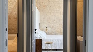 A bedroom with a bed, a small stool, a white pillow, and a brick wall.