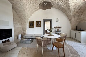 Un salon chaleureux avec un plafond en pierre, une cheminée, un canapé, une table à manger avec des chaises et un coin cuisine.