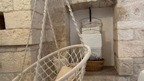 A room with a stone wall, a hanging chair, a basket, and a white towel.