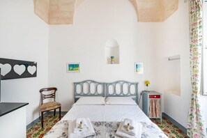 Un dormitorio con una cama, una silla, una mesita y una ventana con cortinas.