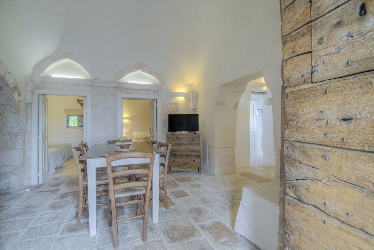 A dining area with a stone floor, wooden furniture, and a television on a wooden cabinet.