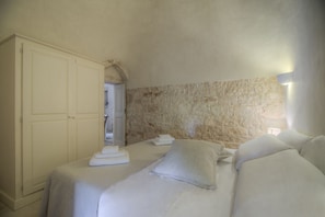Un dormitorio con pared de piedra, una cama con ropa blanca y un armario.