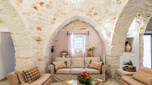 A cozy living room with a stone archway, a sofa set, a coffee table with a flower vase, and a window with curtains. - Trulli Garden Harmony by Rentbeat (Martina Franca)