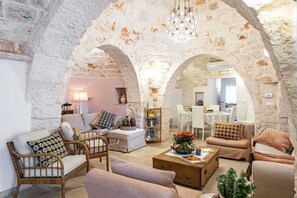 A cozy living room with stone arches, wicker furniture, a coffee table, and a dining area in the background.