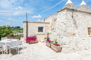 A stone building with a window, a table with chairs, and potted plants.