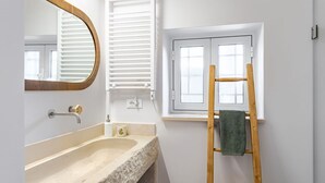 A bathroom with a sink, mirror, towel rack, and window.