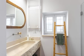A bathroom with a sink, mirror, towel rack, and window.
