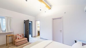 A bedroom with a bed, a wooden stool, a bench, and a door leading to another room.