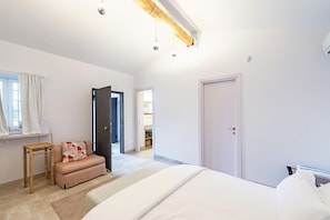 A bedroom with a bed, a wooden stool, a bench, and a door leading to another room.
