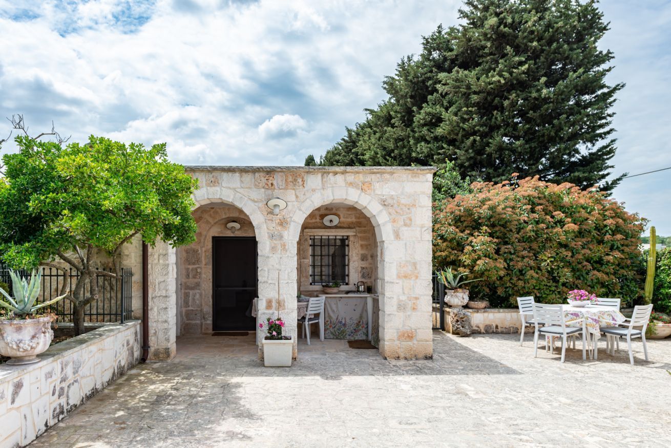 A stone building with arches, a table with chairs, and potted plants.