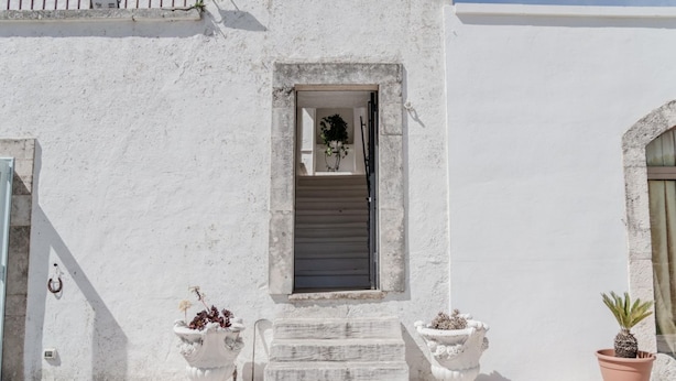 A white building with a small window, a set of stairs leading to the entrance, and two potted plants. - Masseria Carbonico delle Lamie by Rentbeat (Martina Franca)