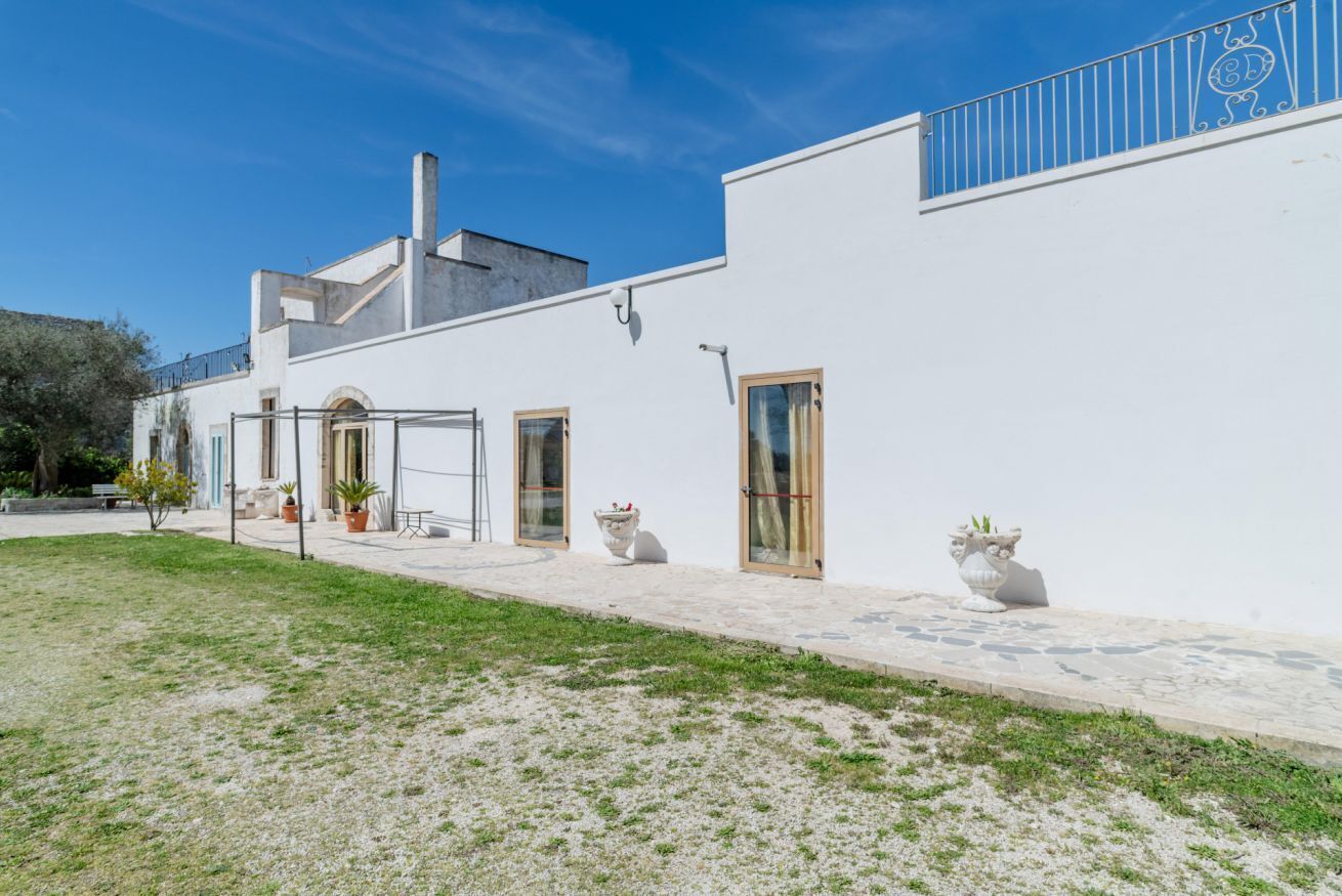 Un bâtiment blanc doté d’un balcon, d’une cheminée et d’une zone pavée agrémentée de plantes en pot.