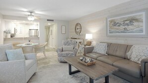 A spacious living area with a beige sofa, patterned armchairs, a coffee table with decorative items, and a large painting on the wall.