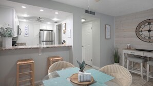 A modern kitchen with white cabinets, a stainless steel refrigerator, and a wooden dining table with wicker chairs.