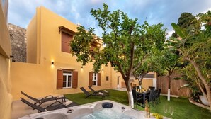 A hot tub in a backyard with a dining table and chairs, surrounded by a yellow building with windows and shutters.
