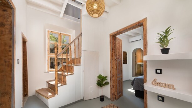 A modern interior with a wooden staircase, a hanging light fixture, and a plant on a shelf.