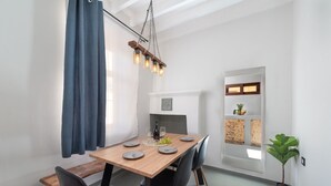 A dining area with a wooden table, black chairs, a hanging light fixture, and a view of a kitchen through an open door.