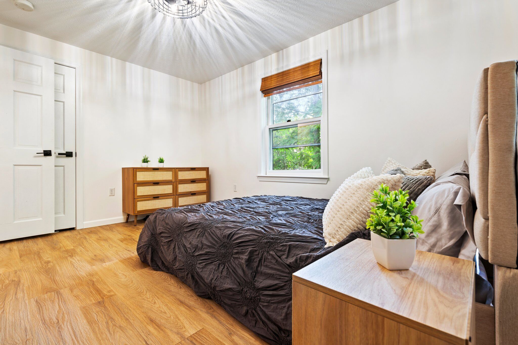 Un dormitorio con una cama grande, un aparador de madera, un ventanal con vistas a zonas verdes y un ventilador de techo.