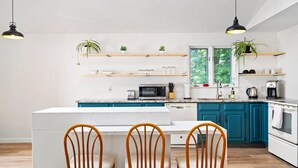 A modern kitchen with teal cabinets, white countertops, a central island with chairs, and pendant lighting. - Scarborough Sanctuary-Cozy retreat close to all local attractions. (Scarborough)