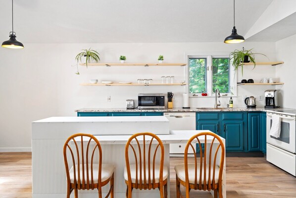 A modern kitchen with teal cabinets, white countertops, a central island with chairs, and pendant lighting. - Scarborough Sanctuary-Cozy retreat close to all local attractions. (Scarborough)