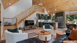 Amplia sala de estar con techo alto, escalera de madera y cocina equipada con electrodomésticos modernos.