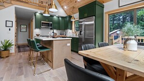 Una cocina moderna con gabinetes verdes, un refrigerador de acero inoxidable y una mesa de comedor de madera con sillas.