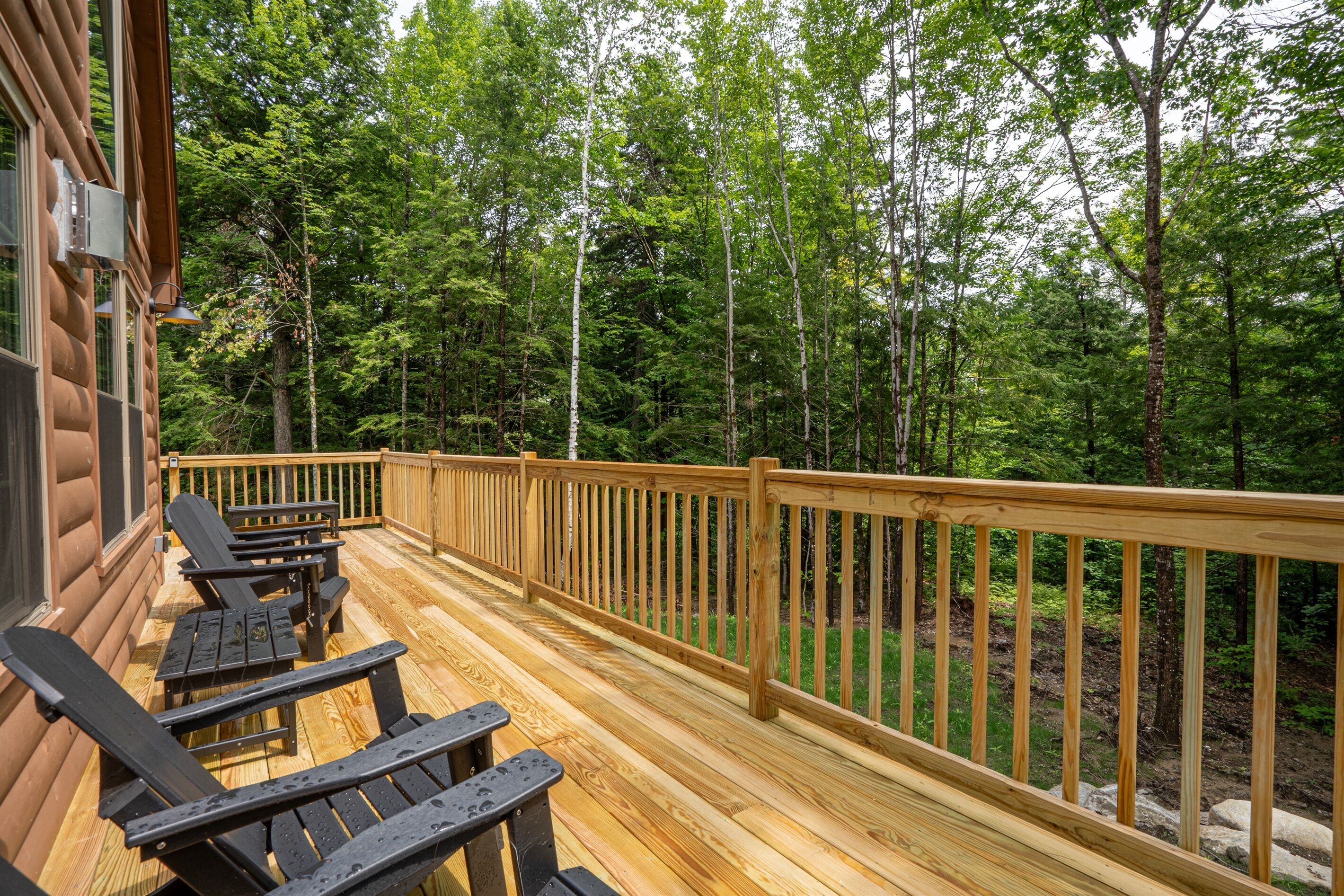 A wooden deck with Adirondack chairs, surrounded by a forest.