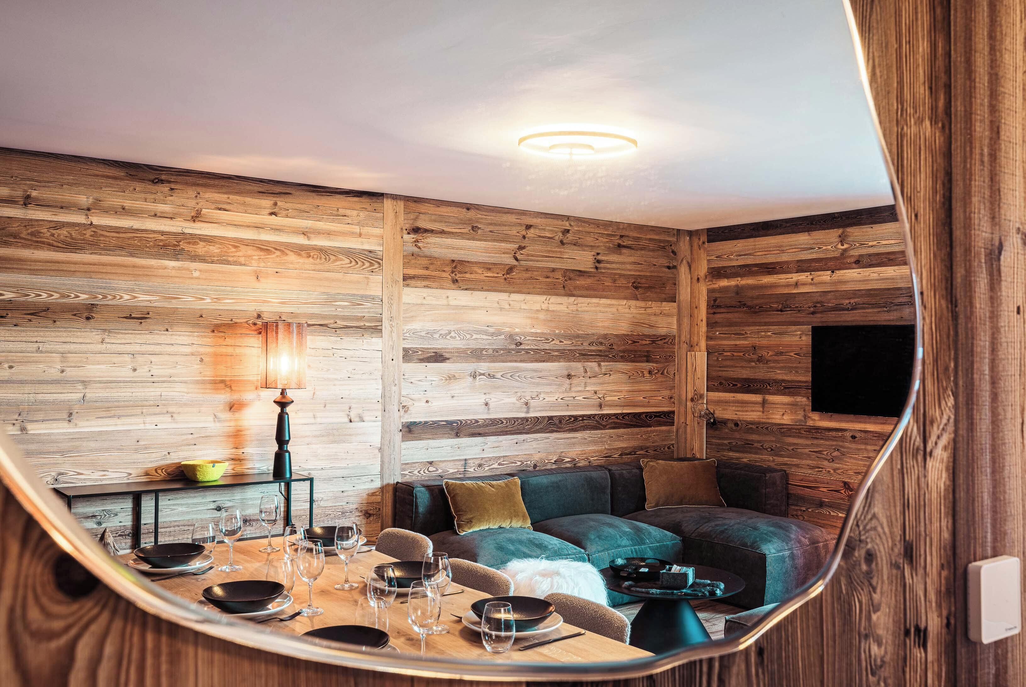 A cozy room with wooden walls, a sofa, a dining table set with glasses and plates, and a flat-screen TV mounted on the wall.