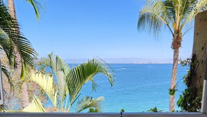 Ein Badezimmer mit Waschbecken, Spiegel und Schränken, mit Blick auf einen Strand mit Palmen und dem Meer.