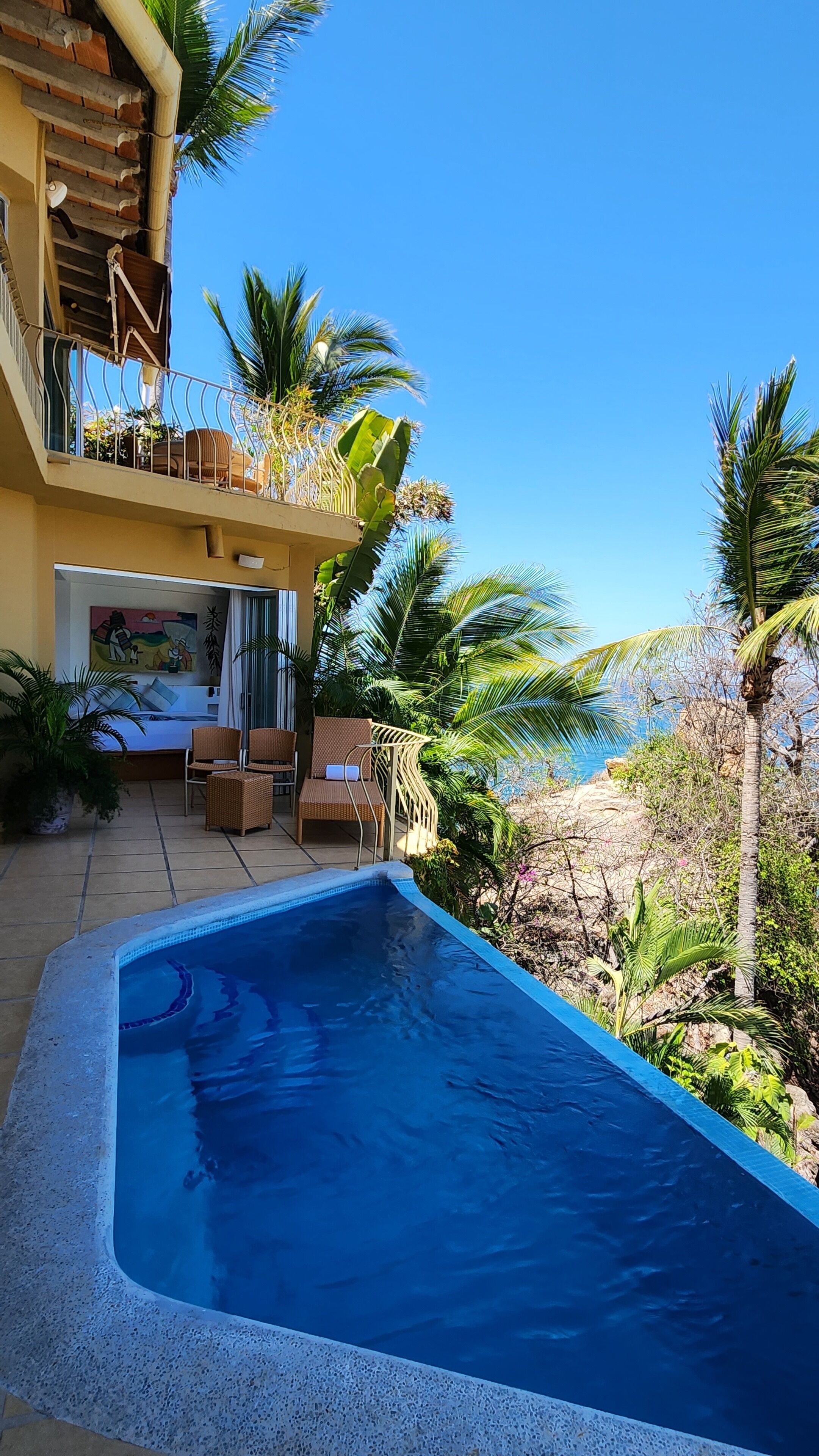 Un espace piscine avec vue sur la mer, un balcon doté de mobilier d’extérieur et un tableau accroché au mur.