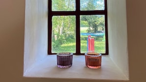 A small window with a white frame and four panes, overlooking a green landscape with trees and a red structure.