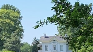 A large, white building with a symmetrical facade, surrounded by a lush green field with grazing sheep.