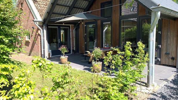 A covered patio area with outdoor seating, potted plants, and a brick building in the background.