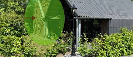 A building with a metal roof, surrounded by greenery and a gravel path.