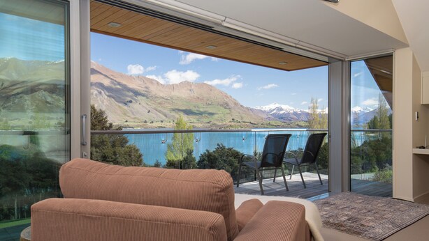 Ein Balkon mit Blick auf einen See und Berge, ausgestattet mit einer Couch und Stühlen.