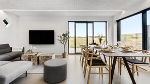 Un salon moderne doté d’un téléviseur à écran plat, d’un canapé, d’une table basse et d’un coin repas avec une table dressée pour six personnes.