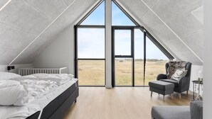 Une chambre avec un plafond en pente, une grande fenêtre, un lit, une chaise et un radiateur.