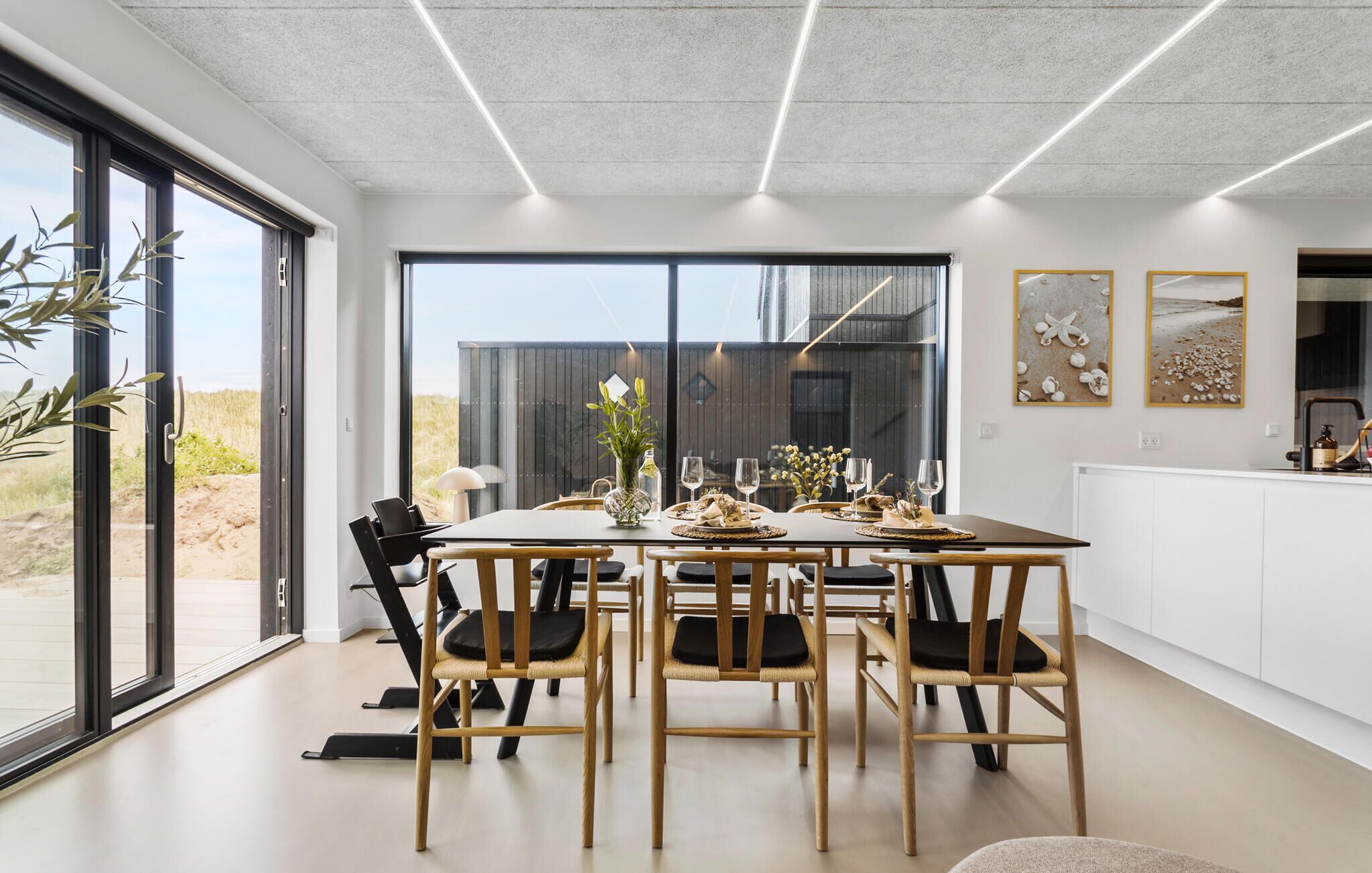 Uma área de jantar moderna com uma mesa grande, cadeiras e vista para o exterior.