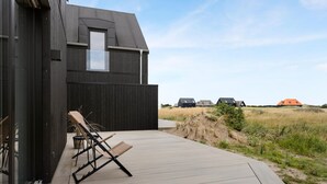 Une maison moderne dotée d’une terrasse en bois, de deux chaises longues et offrant une vue sur le paysage environnant.