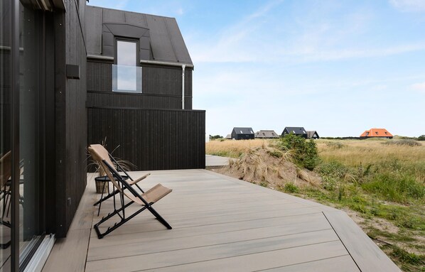 Una casa moderna con terraza de madera, dos sillones de descanso y vistas del paisaje circundante.