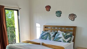 A bedroom with a wooden bed, white bedding, a wooden nightstand, and a view of greenery outside.