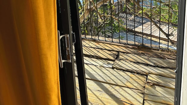 A view through a window with a metal railing, a wooden deck, and trees in the background.