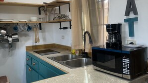 A kitchen with teal cabinets, a double sink, a coffee maker, and a shelf with dishes and utensils.