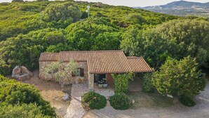 Una casa de piedra con tejado de tejas rodeada de abundante vegetación y colinas al fondo.