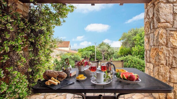 Un área de comedor al aire libre con una mesa dispuesta para una comida, rodeada de follaje y muros de piedra.