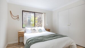 Ein Schlafzimmer mit großem Fenster, einem Bett mit grüner Decke und einem weißen Kleiderschrank.