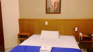 A hotel room with a large bed, a wooden headboard, a nightstand with a phone, and a framed picture on the wall. - Hotel Imigrantes LTDA (São Pedro)